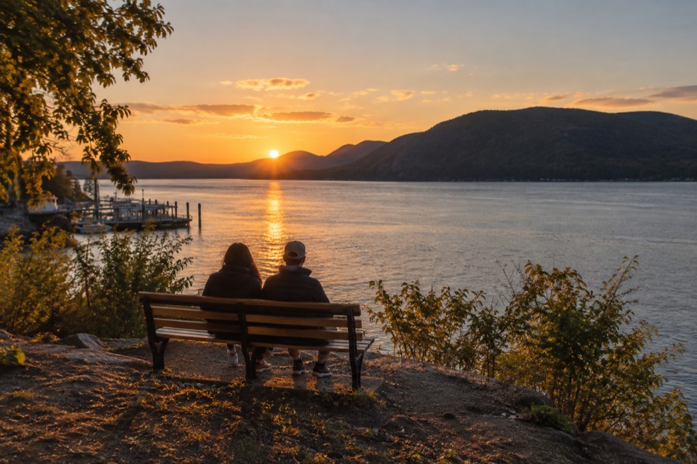 A riverside park bench facing wide water and distant mountains at golden hour