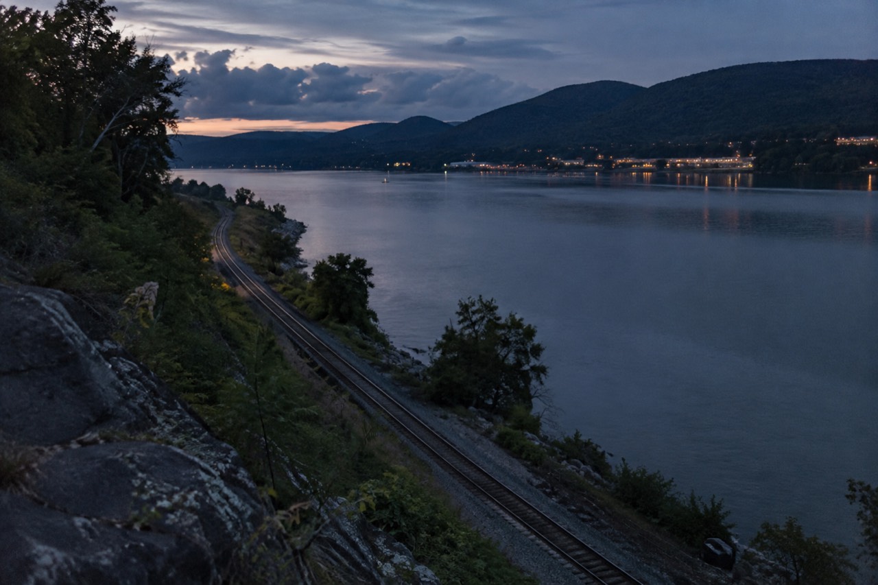 Rolling forested hills along the Hudson River with a railroad track running beside the water
