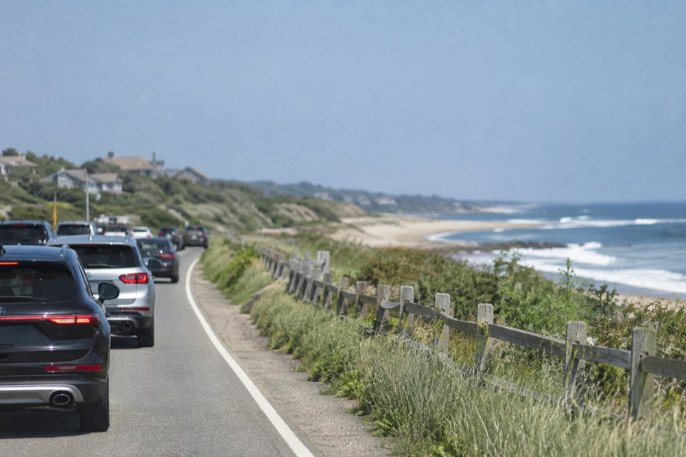 Traffic slowly moving along a two-lane highway lined with beach grass and wooden fencing