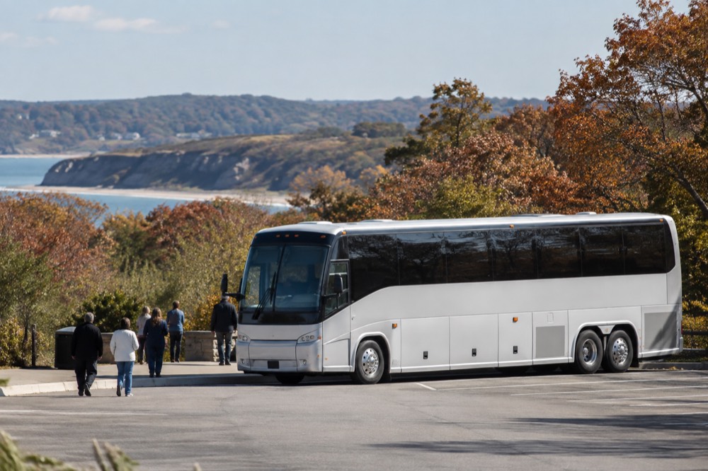 A coach bus parked at a rest stop with autumn trees and rolling hills behind it
