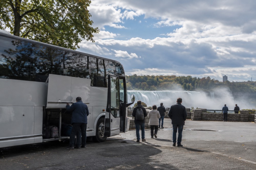 A coach bus parked at a rest stop on a highway with trees along the horizon