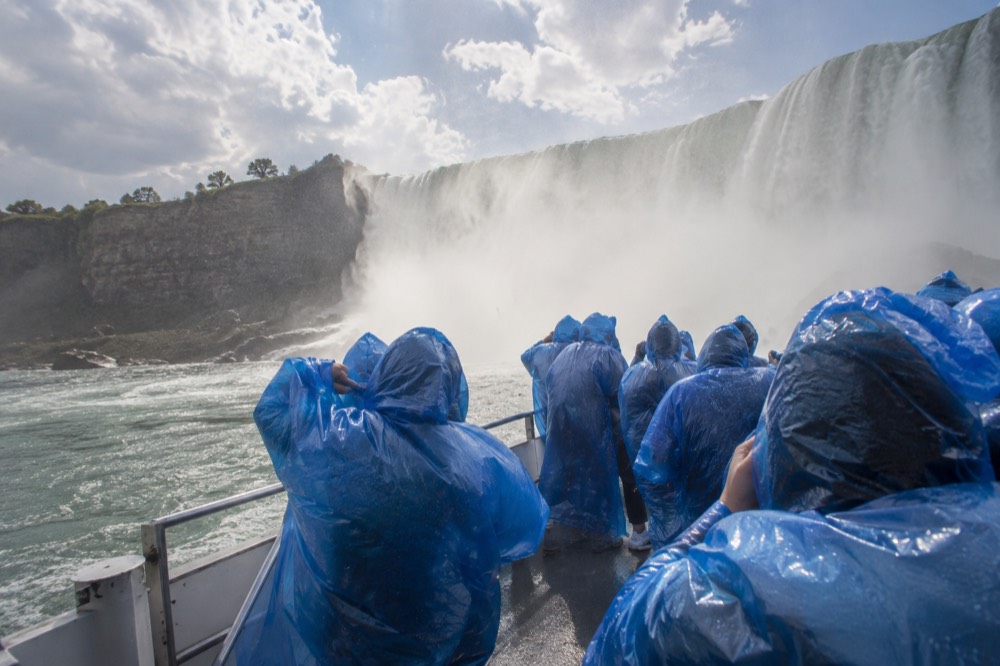 Passengers in blue ponchos standing on a boat deck near the base of a waterfall
