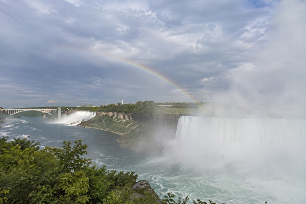 Rainbow appearing in the mist above a waterfall with trees along the riverbank