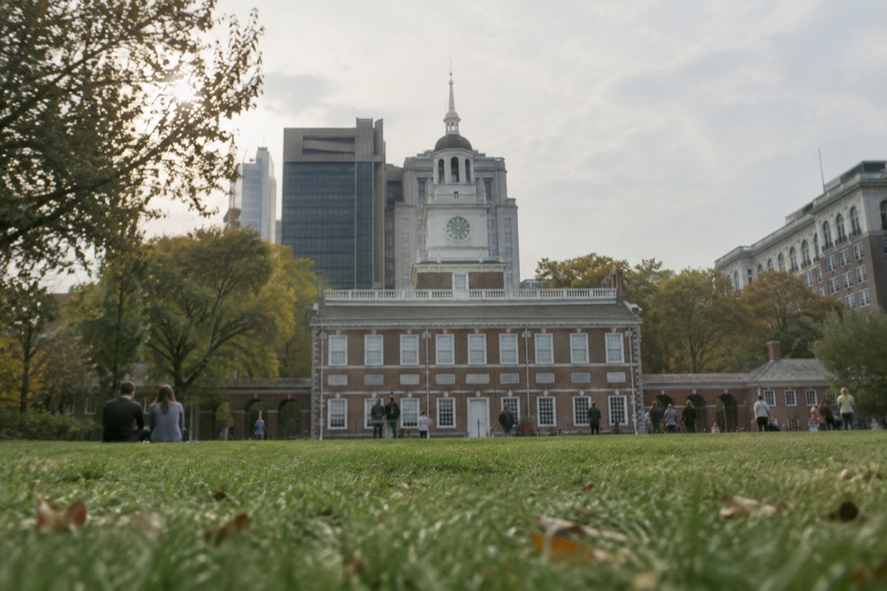 Independence Hall's red brick facade and white bell tower seen from the green in front of it