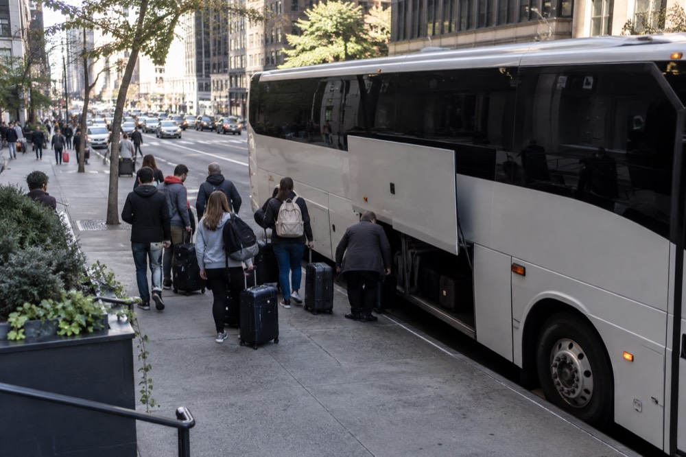 A long-distance coach parked at a curb in Manhattan with passengers loading bags