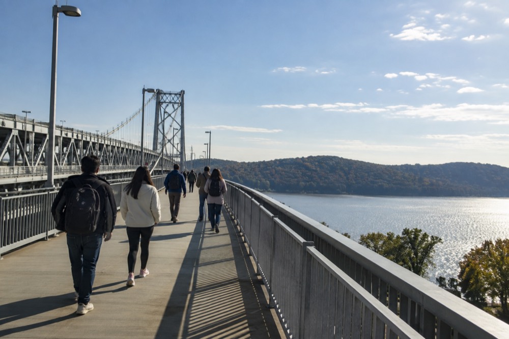 Visitors walking a wide elevated bridge deck high above a river valley