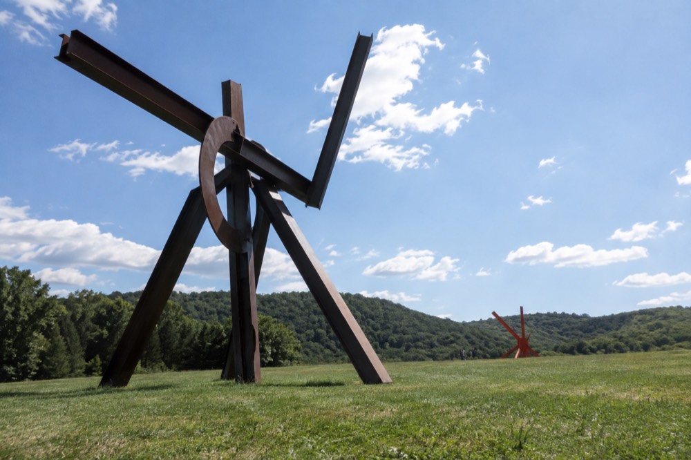 Large abstract sculptures standing in open rolling fields with wooded hills behind them