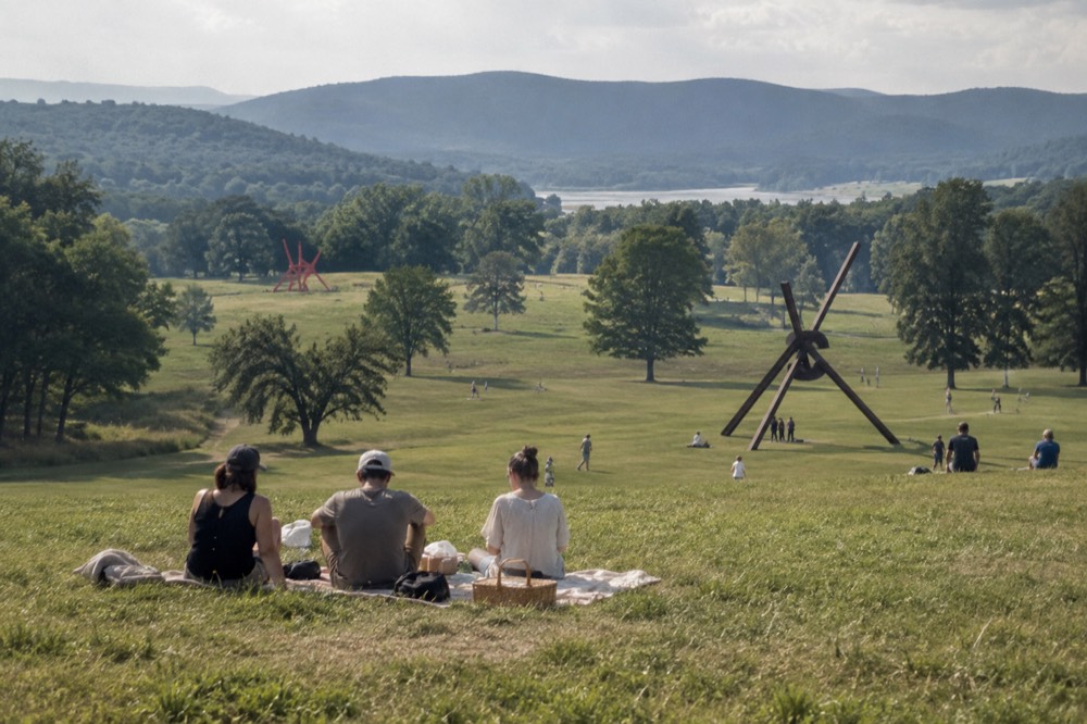 People sitting on a grassy slope having a picnic with sculptures in the distance