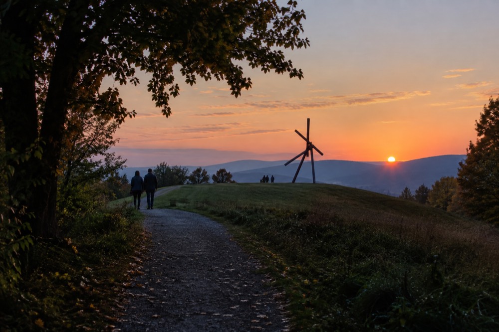 A quiet gravel path at dusk leading toward a solitary sculpture silhouetted against a fading sky