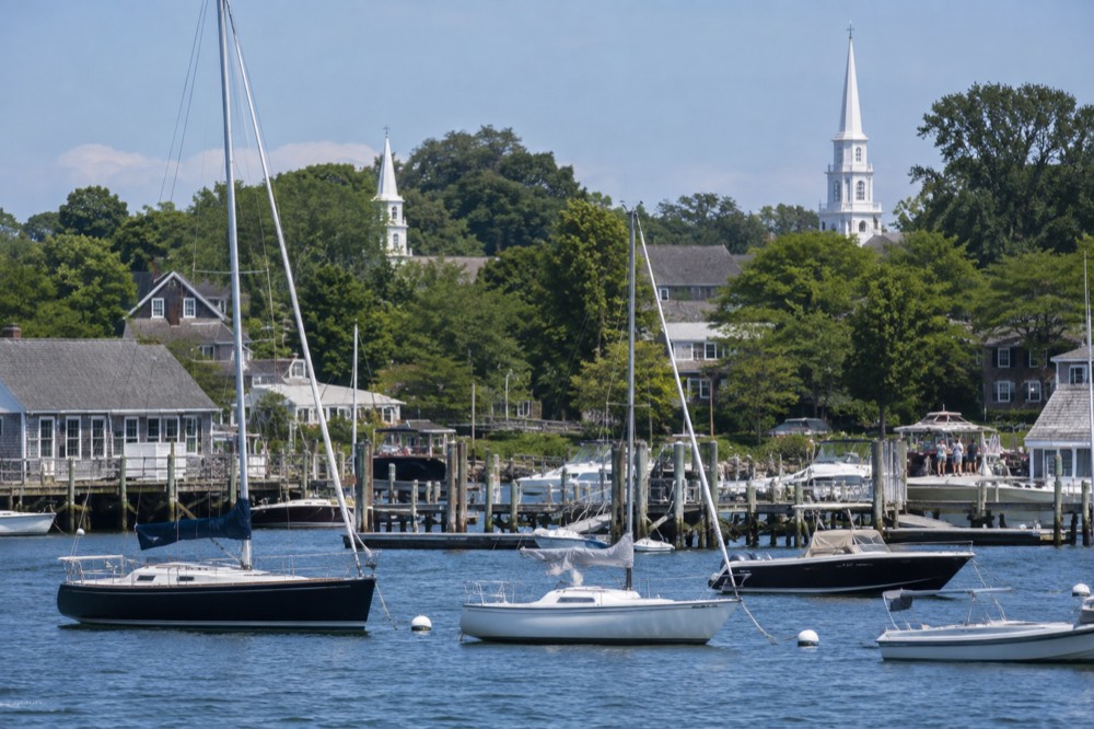 Sailboats moored in a small harbor with wooden docks and white church steeples beyond