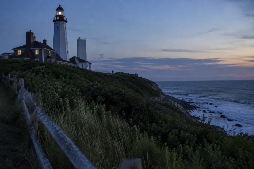 A white lighthouse on a grassy bluff above the ocean at the eastern tip of Long Island