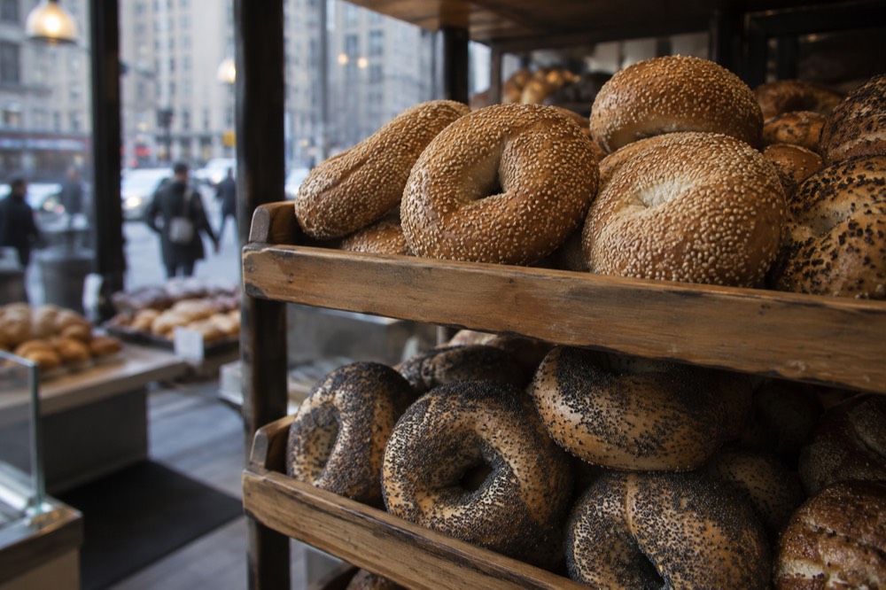 Sesame and poppy seed bagels in wooden trays stacked inside a bakery