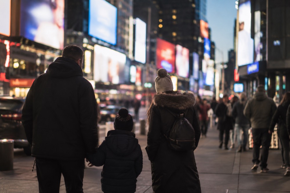 A family walking through a bright theater district street at night