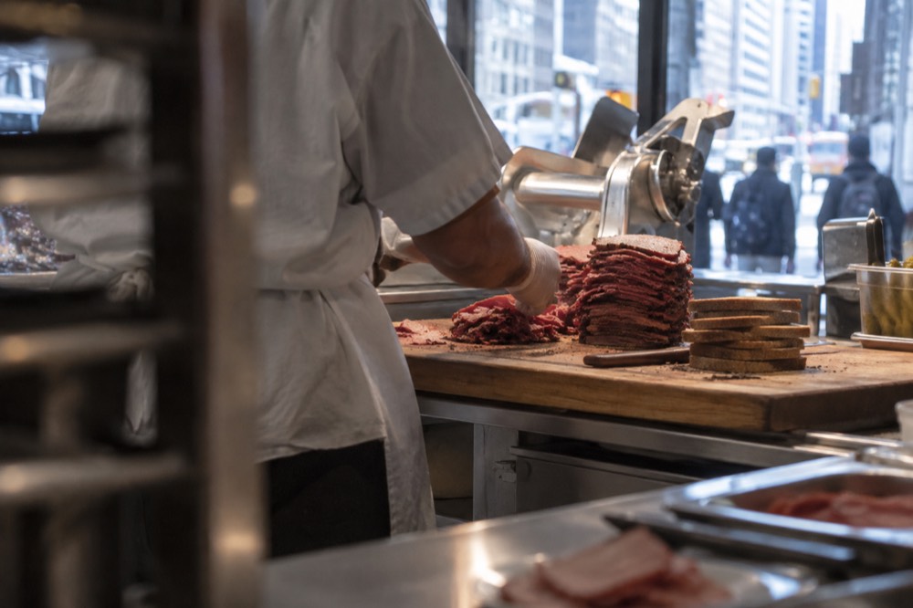 Sliced rye bread and a stack of cured meat on a wooden cutting board in a deli kitchen