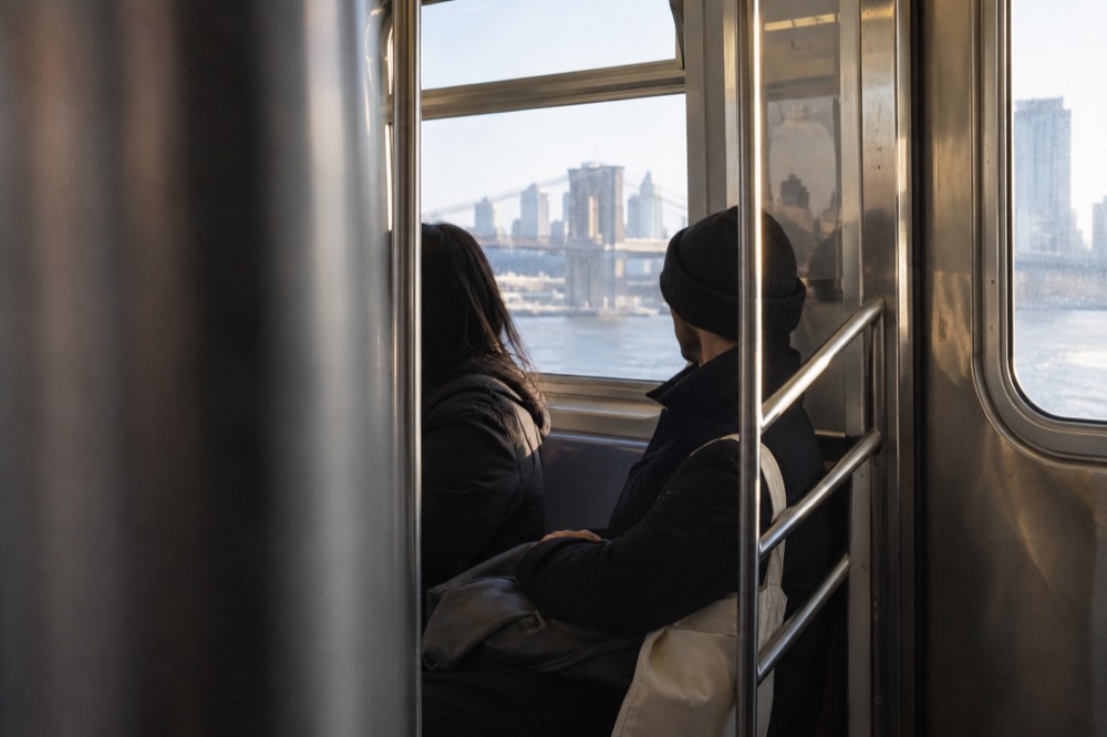 Two people riding a New York subway train seated near the door on a weekend afternoon