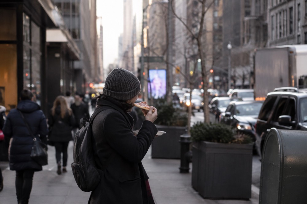 A person eating a folded pizza slice on a New York sidewalk