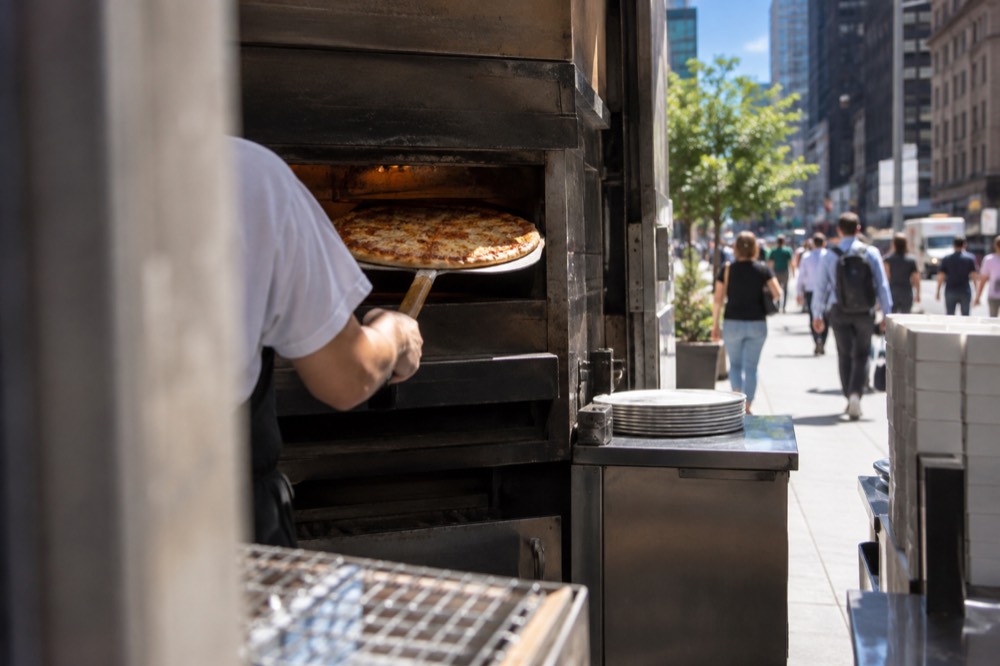 A fresh cheese pizza being lifted from a deck oven with a long peel