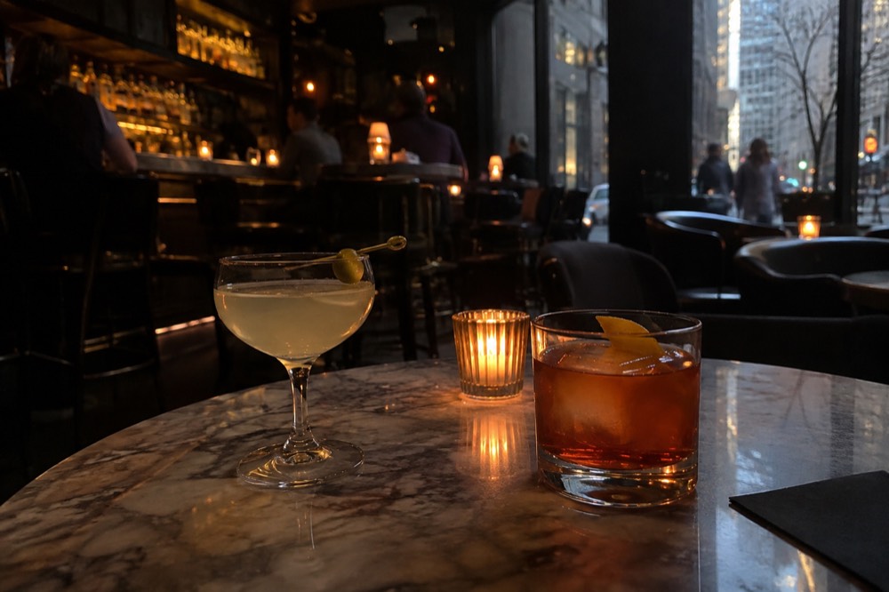 Two cocktails on a small marble table in a dark bar