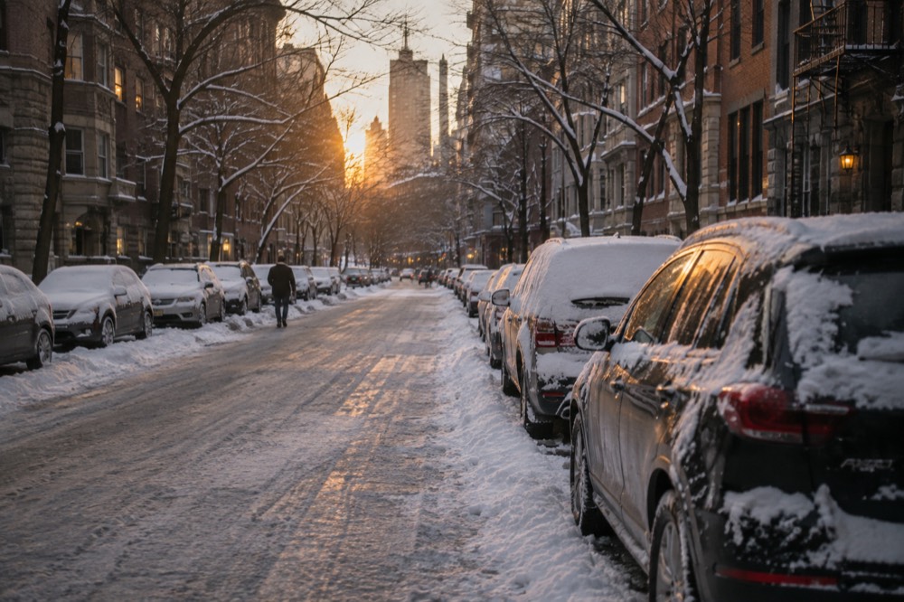 Snow covering a quiet street in Manhattan with parked cars and bare trees