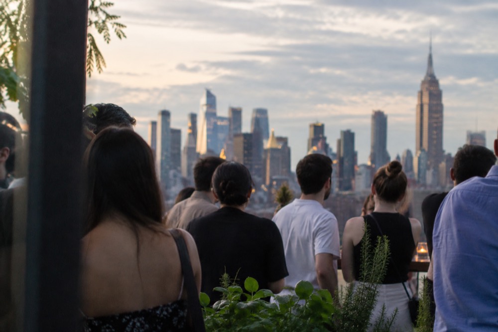 A rooftop crowd overlooking the Manhattan skyline on a warm summer evening