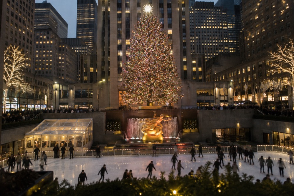 The Rockefeller Center Christmas tree lit at night with skaters on the ice rink below