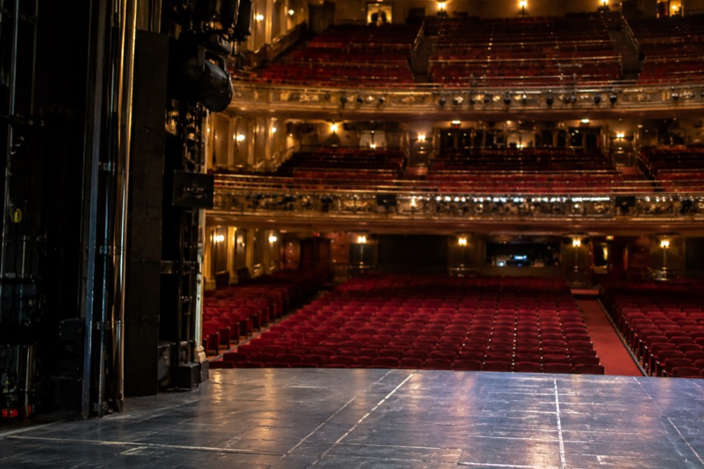 An empty Broadway auditorium seen from the stage with red velvet seats in rows