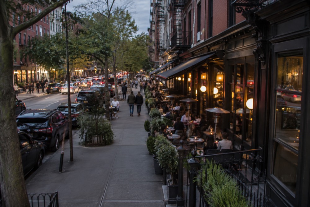 A busy sidewalk table scene outside restaurants in the West Village at dusk