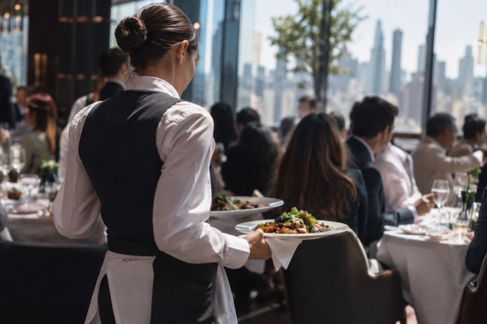 A server carrying plates through a crowded upscale New York dining room