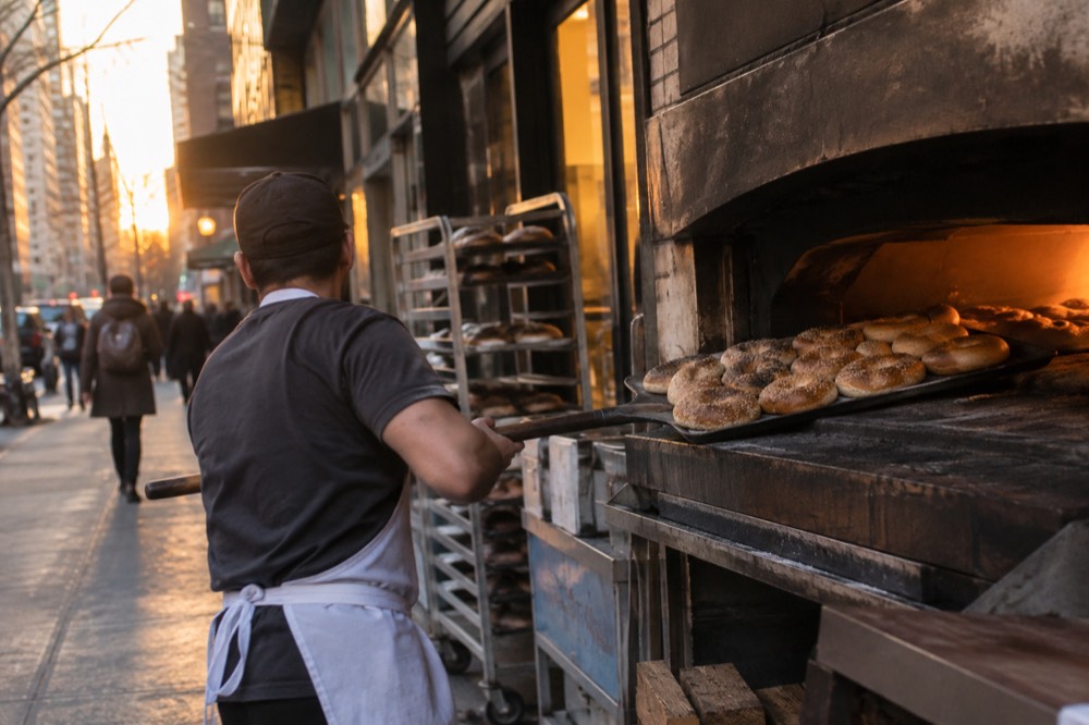 Bagels being pulled from a wood oven at a busy shop