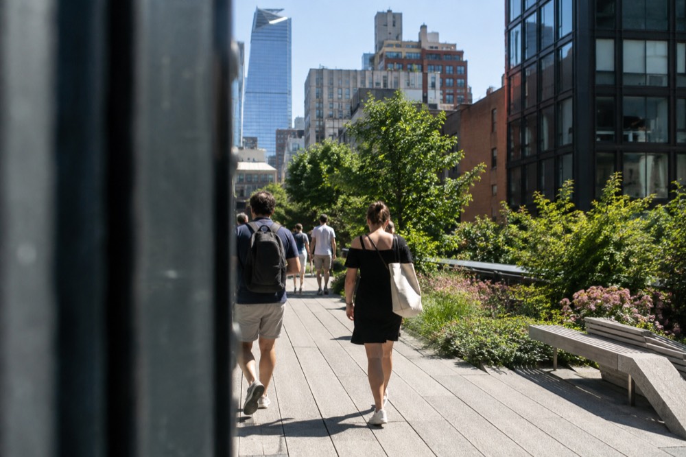 Visitors walking the elevated High Line park between green plantings and city buildings