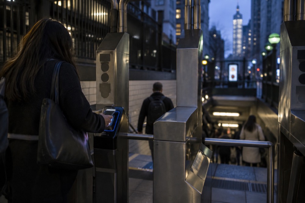 A rider tapping a phone at a subway turnstile OMNY reader