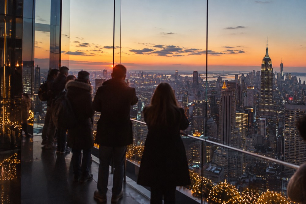 Manhattan skyline at dusk seen from a glass observation deck with holiday lighting below