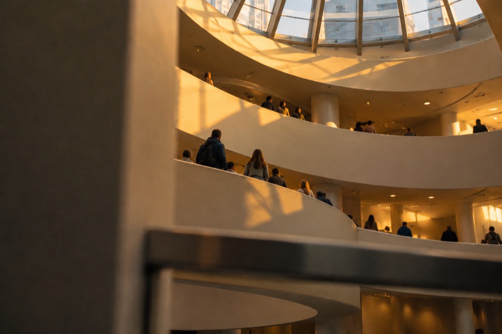 Visitors ascending the spiral ramp of a modern art museum under a glass skylight