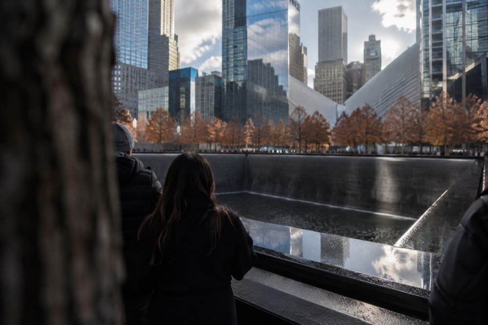 People pausing at the edge of a large reflecting pool memorial in Lower Manhattan