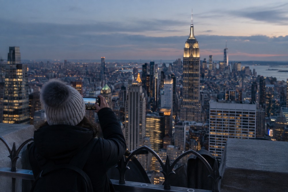 A sightseer photographing the Manhattan skyline from an elevated observation deck