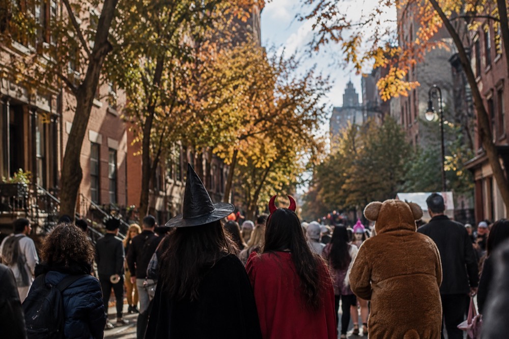 A costumed crowd gathered on a Greenwich Village street beneath orange autumn light