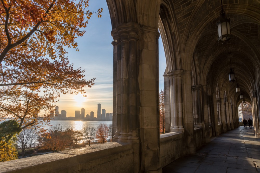 A medieval-style cloister building with stone arches overlooking the Hudson River in autumn