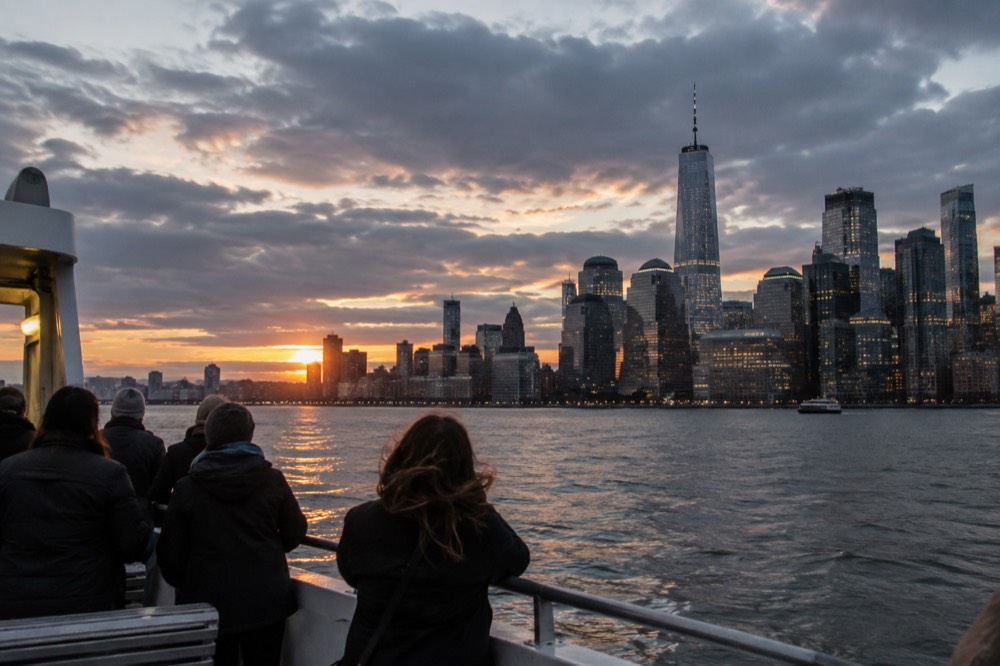 A ferry crossing New York Harbor toward Lower Manhattan at dusk