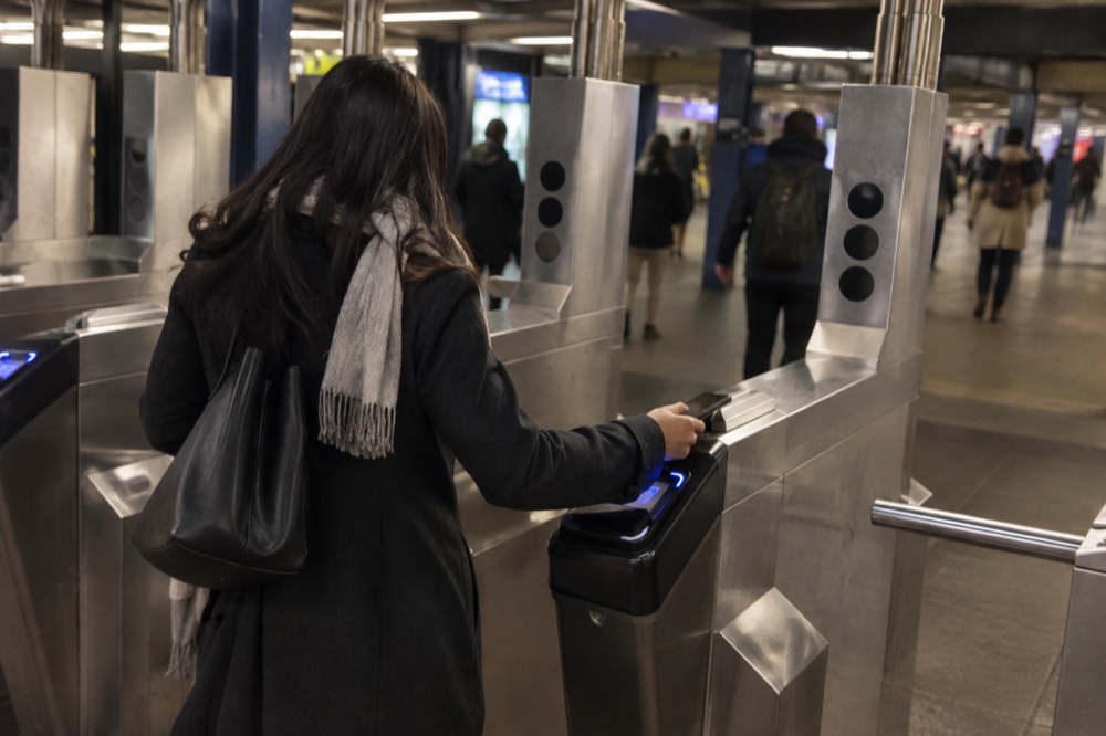A woman tapping her phone on an OMNY reader at a subway turnstile