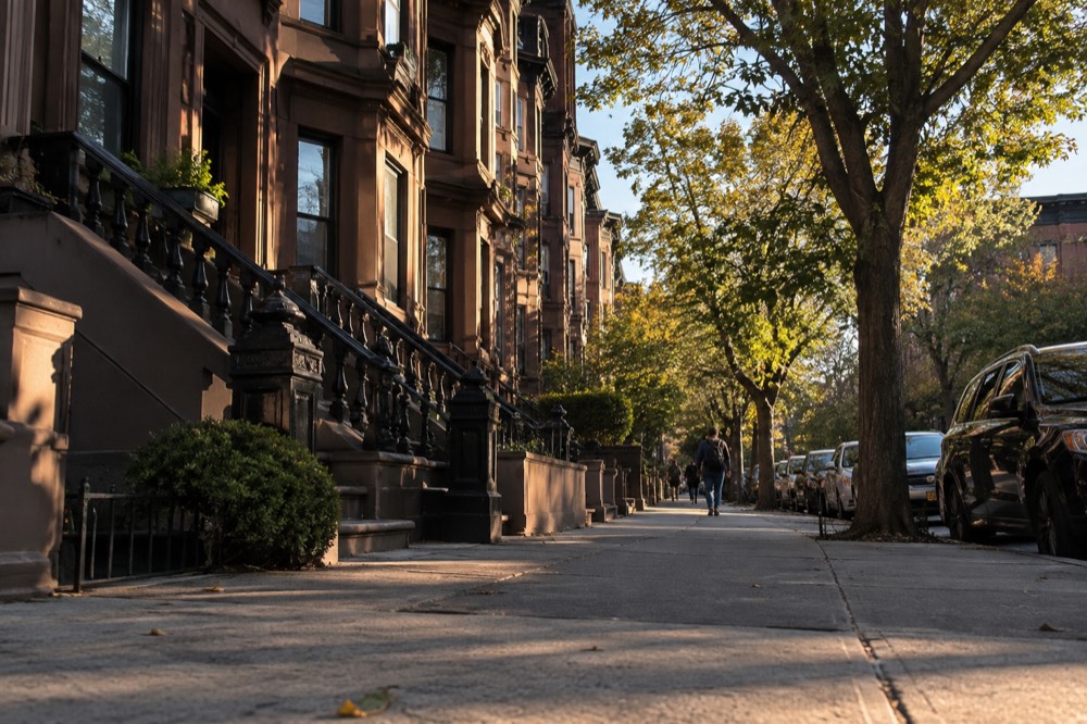 A quiet residential street in Brooklyn with brownstone buildings in late afternoon light