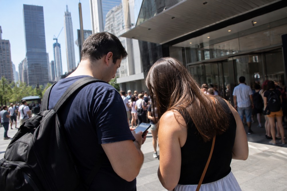 A couple comparing ticket prices on a phone outside a New York attraction entrance