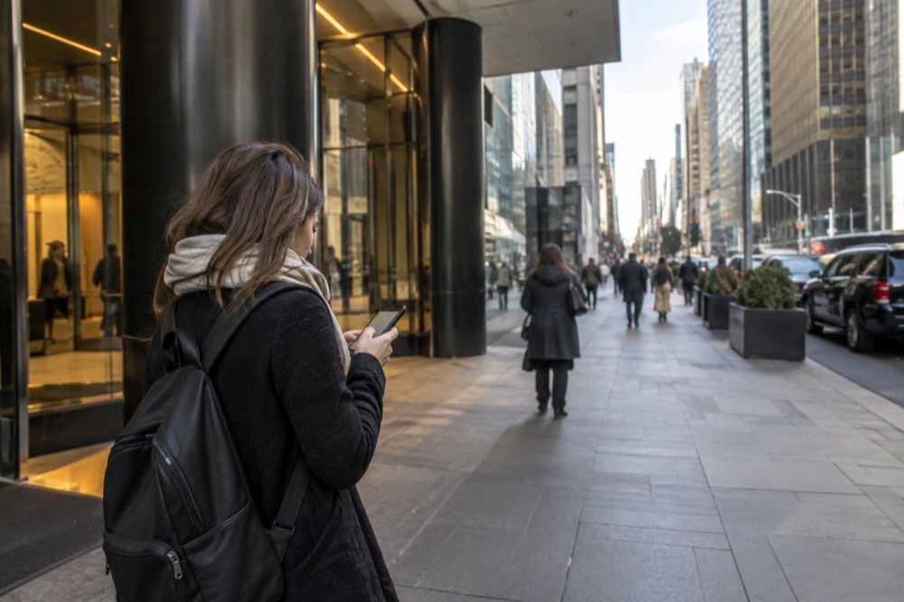A traveler checking a phone app while waiting outside a skyscraper entrance