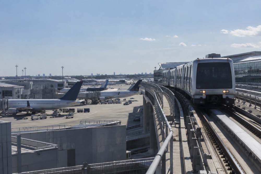 The AirTrain approaching a JFK terminal station with planes parked at gates behind it