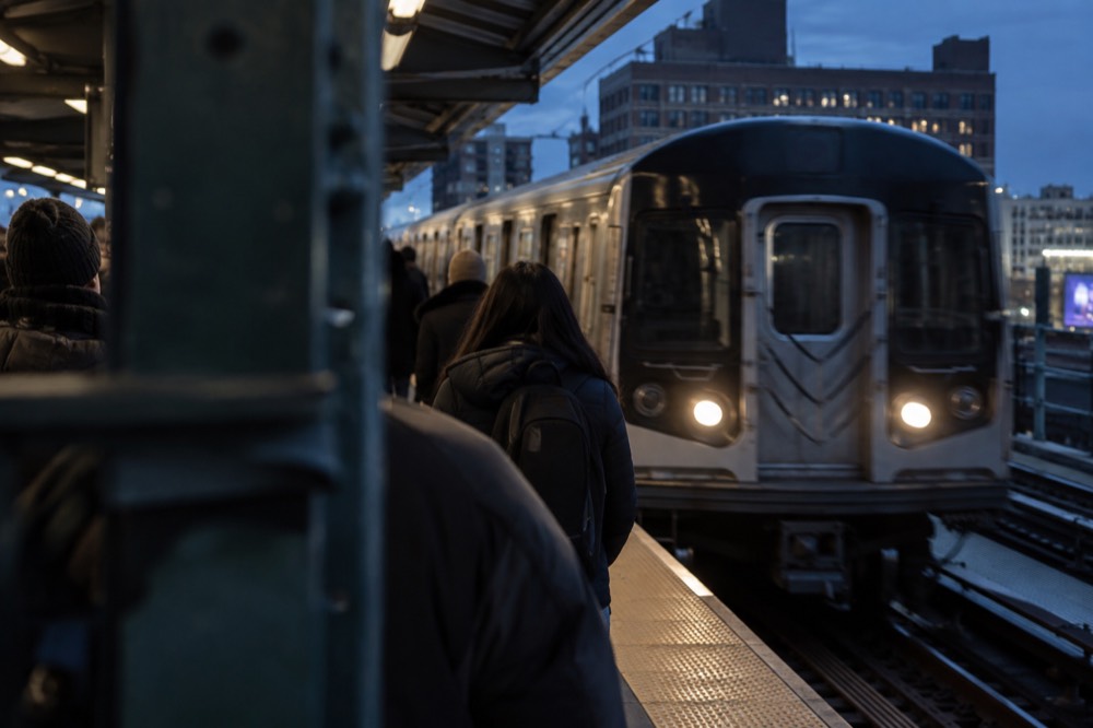 A subway platform at Jamaica station with an E train arriving and passengers boarding
