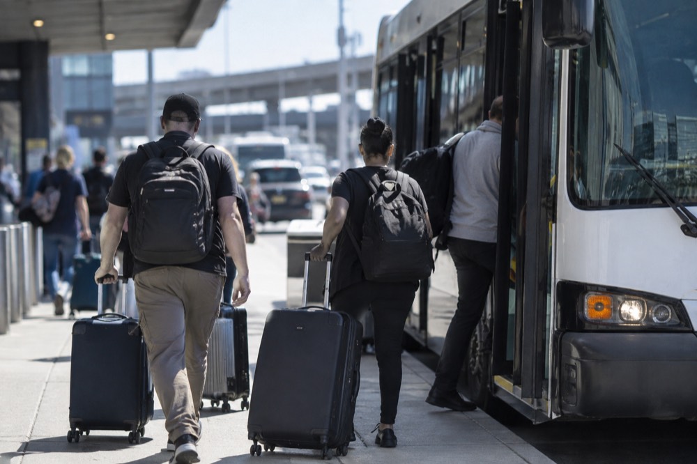 Travelers with suitcases boarding a public bus at a LaGuardia terminal curb