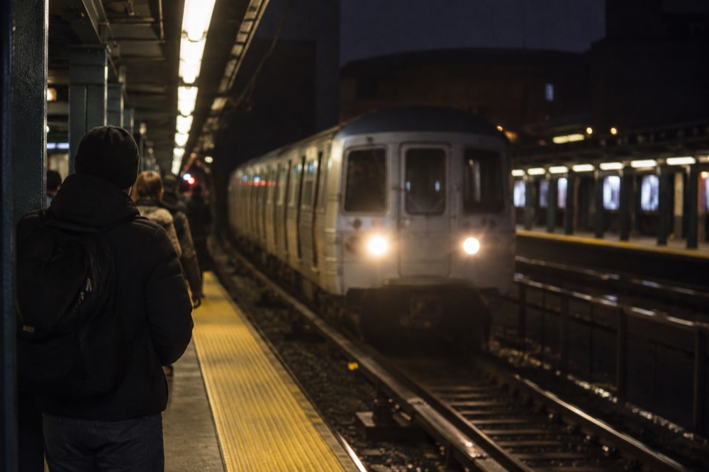 A subway platform in Queens at night with a train arriving