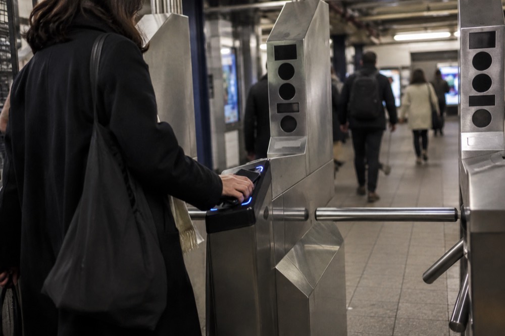 A subway turnstile in a New York station with a rider tapping a phone on the OMNY reader