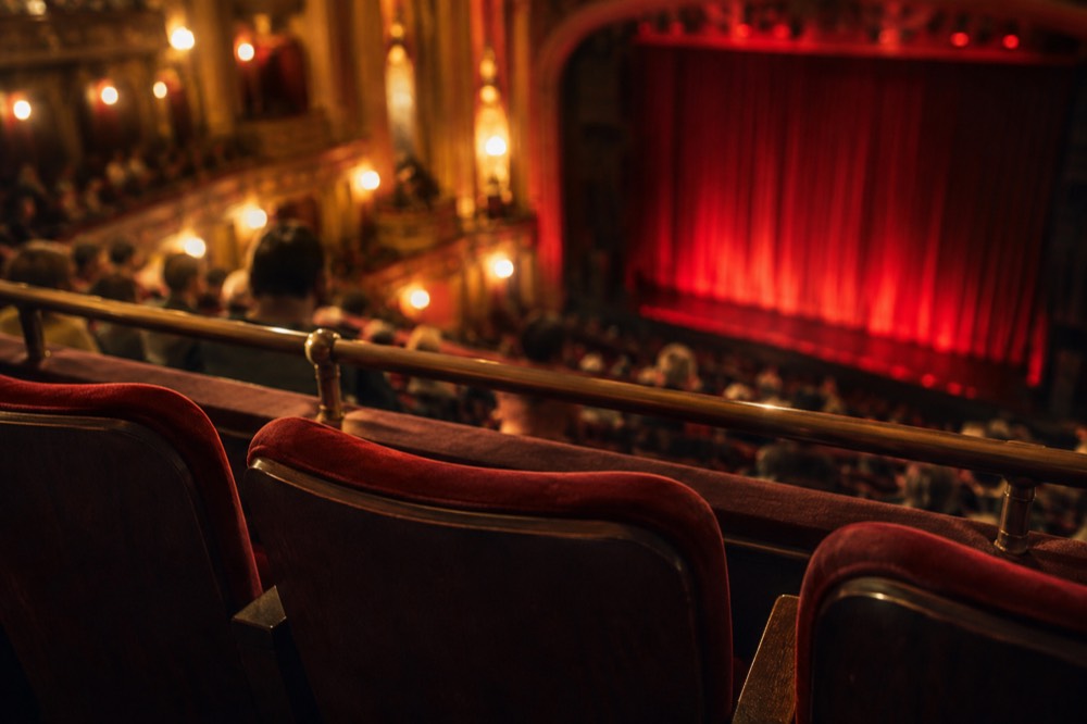 Close-up of theatre seats in the mezzanine overlooking a stage lit in deep red
