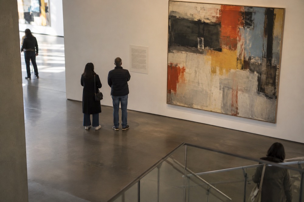 Museum visitors reading wall text beside a large abstract painting
