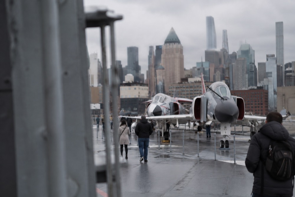 An aircraft carrier flight deck with vintage jet aircraft on display by the river